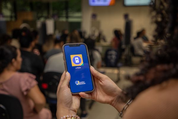 As mãos seguram um celular onde está aberto o Aplicativo e-Título