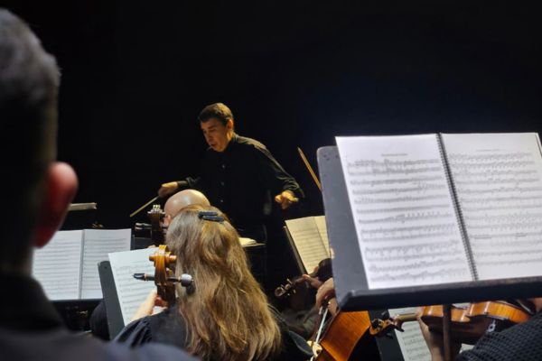 Maestro regendo uma orquestra e um dos músicos o acompanhando