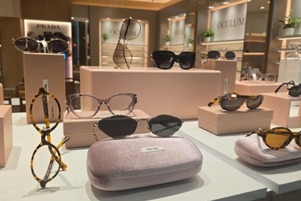 òculos escuros e óculos de grau dispostos sobre o porta-óculos, em exposição em uma mesa