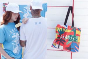 Um casal utilizando as peças que apresentam estampas que valorizam a brasilidade e refletem a diversidade cultural do país, reforçando o compromisso da iniciativa com a produção local e a geração de impacto social positivo.