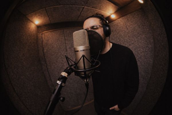 Rosivaldo Cordeiro, artista, está em um estúdio de música gravando, à sua frente há um microfone