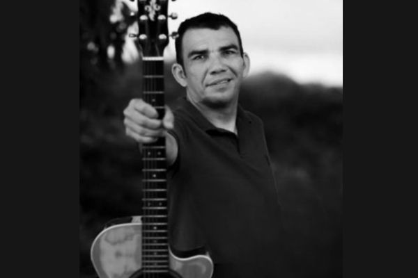 cantor Fábio Sill segurando um violão, ele está vestindo uma camisa preto e tem um sorriso no rosto