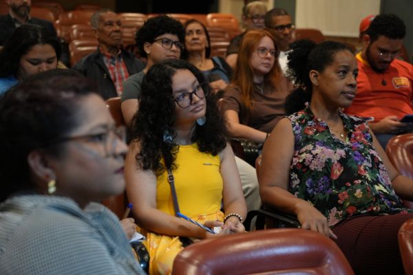 Pessoas atentas e sérias, assistindo um espetáculo, em uma plateia