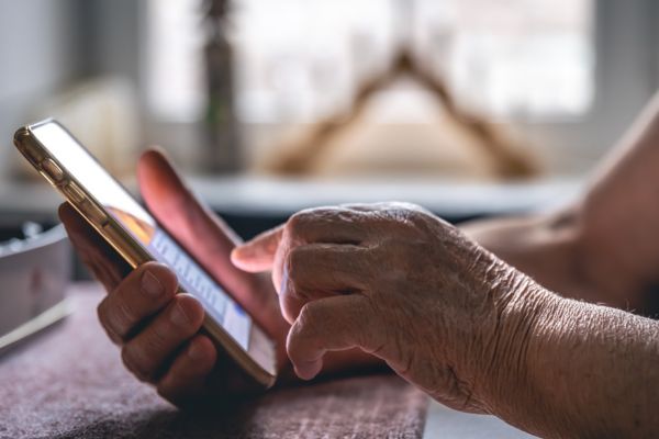 Um pessoa idosa segurando e utilizando um celular